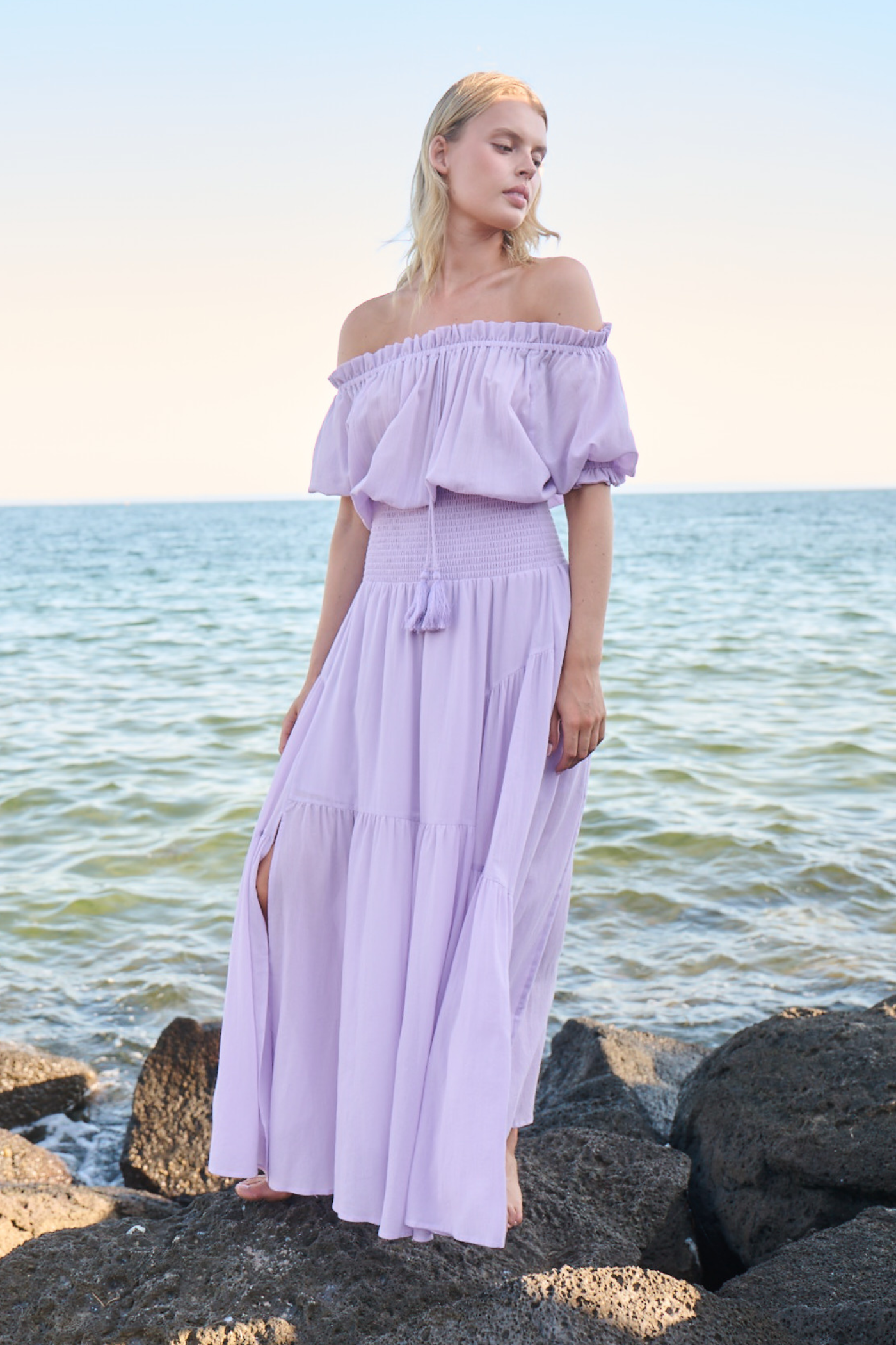 Model on rocks posing in long purple dress